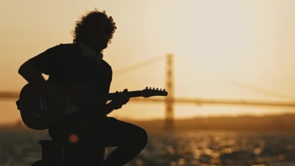 Silhouette Eines Mannes Der Bei Sonnenuntergang Gitarre Spielt Während Damm — Stockvideo