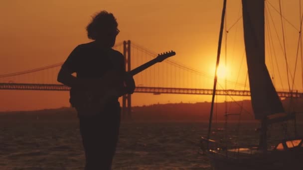 Sylwetka Człowieka Hipstera Stojącego Nabrzeżu Grającego Gitarze Przy Jasnym Pomarańczowym — Wideo stockowe