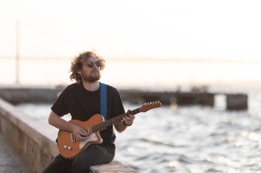Rıhtımda oturup gitar çalan bir hippi. Orta çekim