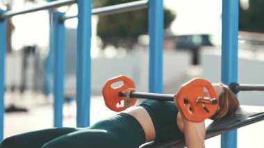 Yetişkin fitness kadını spor simülatörüne uzanmış halterini kaldırarak ellerini çalıştırıyor. Orta çekim