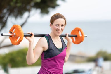 Omzunda dambılla makyajsız, gülümseyen yetişkin bir atletik kadın. Portre