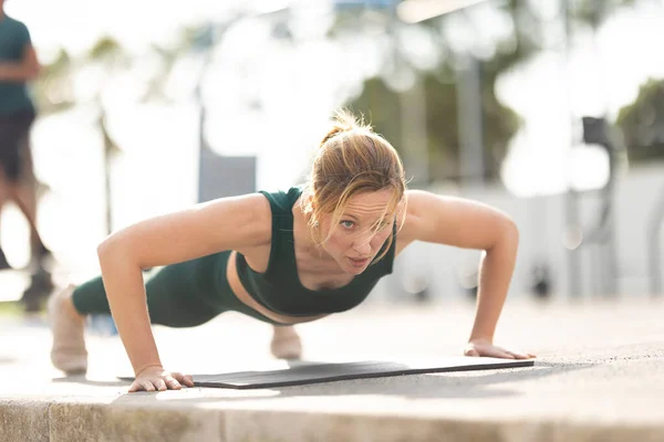 stock image Adult sportive woman with no make up doing push ups on yoga mat outdoors. Mid shot