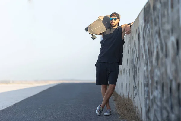 stock image Adult attractive man standing by the wall holding a skateboard. Mid shot