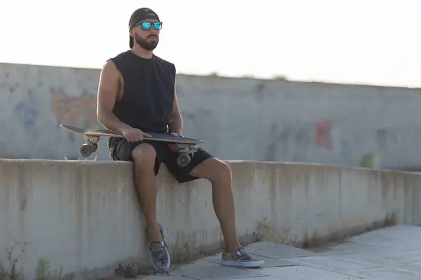 スケートボードを保持するコンクリート階段に座って大人の魅力的な男 ミッドショット — ストック写真