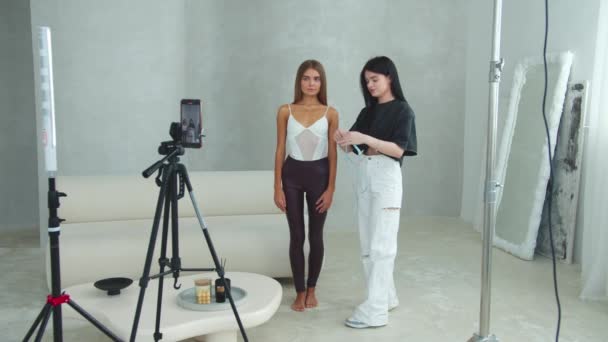 スリムなモデルの近くに立って健康と体重減少についてのビデオブログのためのビデオを撮影し 彼女の体の測定を取る若い女性 ミッドショット — ストック動画
