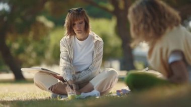 İki kadın arkadaş birlikte vakit geçiriyorlar. Yaz parkında resim yapıp konuşuyorlar. Orta çekim