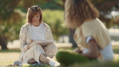 İki kadın arkadaş birlikte vakit geçiriyorlar. Parkta resim yapıp konuşuyorlar. Orta çekim
