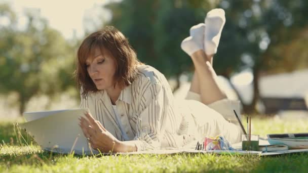 Взрослая Женщина Лежит Одеяле Цветущем Парке Рисует Своем Альбоме Средний — стоковое видео