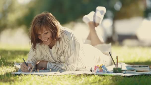 Взрослая Женщина Лежит Одеяле Цветущем Парке Рисует Альбоме Средний Выстрел — стоковое видео