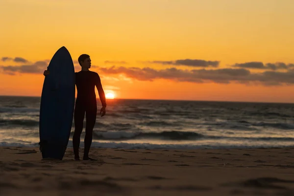 Açık Turuncu Günbatımında Elinde Sörf Tahtası Olan Dalgıç Kıyafetli Bir — Stok fotoğraf