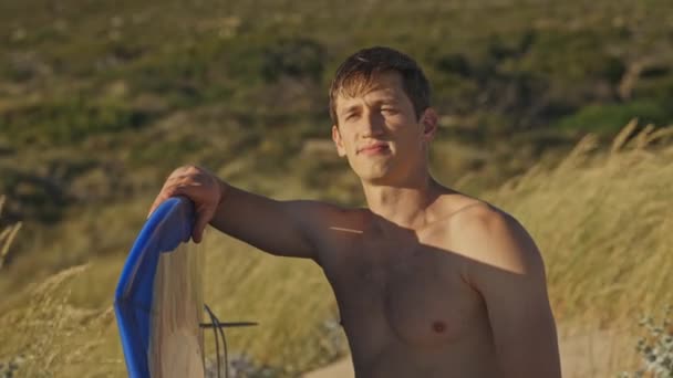 Uomo Senza Maglietta Seduto Uno Sfondo Erba Ondulante Possesso Surf — Video Stock