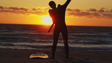 Adamın biri dalgıç kıyafetini okyanusa ve parlak bir günbatımına doğru çekiyor. Orta çekim
