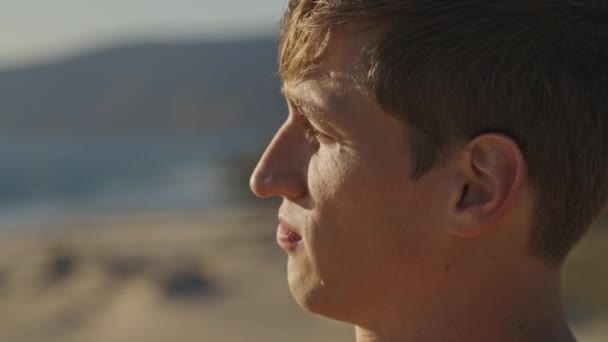 Het Penetrante Gezicht Van Een Jongeman Het Strand Bij Zonsondergang — Stockvideo