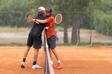 Dostça bir tenis maçı. Rakipler kalenin üstünde sarılıyor. Orta çekim