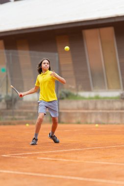 Dostça bir tenis maçı. Sarı tişörtlü bir çocuk topu alıyor. Dikey çekim