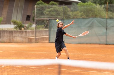 Siyah tişörtlü bir çocuk kortta tenis oynuyor. Orta çekim