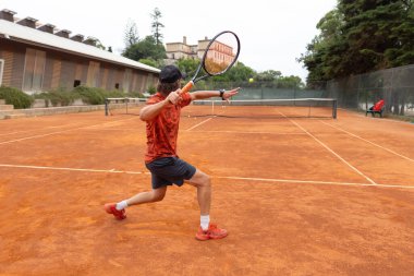 Sahada tenis oynayan kırmızı tişörtlü yetişkin bir adam. Orta çekim