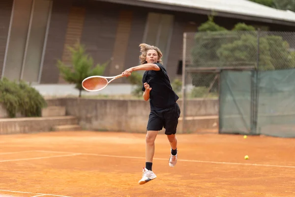 一个身穿黑色T恤衫的少年在球场上打网球 在运动的框架中 回击球 — 图库照片