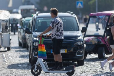 Lizbon, Portekiz - 24 Haziran 2023: Gökkuşağı renkli LGBT çantalı bir adam elektrikli scooter kullanıyor. Orta çekim
