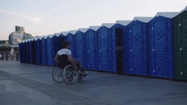 Umumi tuvaletlerin önünde tekerlekli sandalyedeki bir adam. Orta çekim