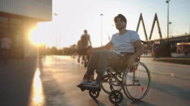 Tekerlekli sandalyedeki bir adam gün batımında basket topu yakalar. Orta çekim