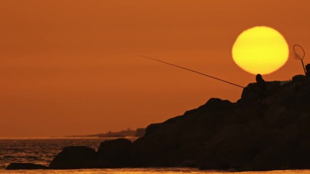 Homem Senta Nas Rochas Pesca Pôr Sol Meio Tiro — Vídeo de Stock
