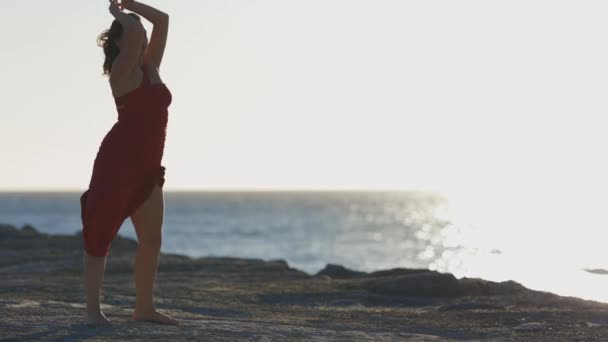 穿着红衣服的优雅的年轻女子在海边的石板上跳舞 — 图库视频影像