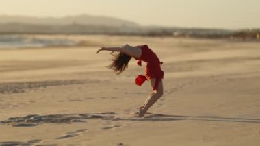 Kırmızı elbiseli zarif duygusal kadın kumda dans ediyor. Orta çekim