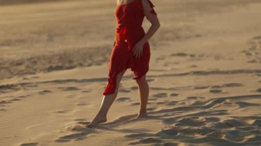 Çıplak ayakla kumda yürüyen zarif bir kadın. Orta çekim