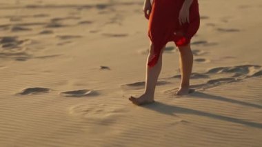 Kırmızı elbiseli kadın kumda yürüyor. Orta çekim
