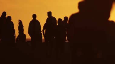 Yavaş çekimde turuncu gün batımında yürüyen insanların bulanık siluetleri. Orta çekim