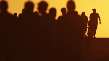 Gün batımında yavaş çekimde yürüyen insanların bulanık siluetleri. Orta çekim
