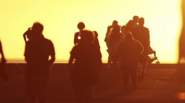 Gün batımında yavaş çekimde yürüyen insanların bulanık siluetleri. Orta çekim