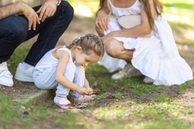 Park yerinde bir aile, çimenlere bakan küçük bir kız ve ailesi onu izliyor. Orta çekim