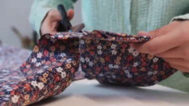 Bir kadın çiçek kumaşındaki desenleri makas kullanarak kesiyor. Orta çekim