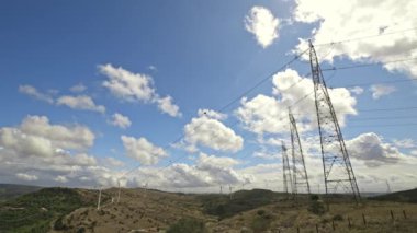 Bir elektrik iletim kulesi, kabarık beyaz bulutlardan oluşan bir zemin üzerine kuruludur..