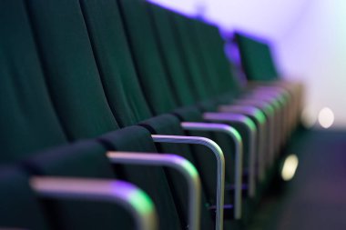 Boş yeşil döşemeli koltuklar dizisi. Muhtemelen bir tiyatro veya konferans salonunda..