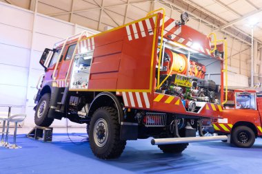 Kırmızı ve turuncu büyük itfaiye aracı - off-road, önemli bir vinç kolu ile donatılmış.
