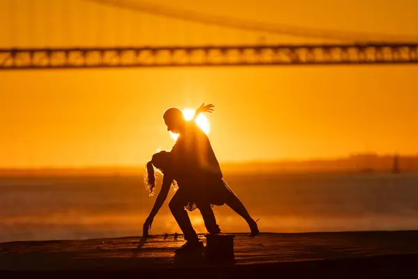 The setting sun casts a warm glow on a dancing couples silhouette, with the bridge adding depth to the scene.