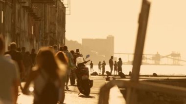Portekiz, Almada 'da nehir kenarındaki parkta yürüyen isimsiz erkek ve kadın kalabalığı - gün batımı, altın saat