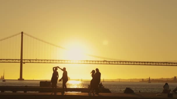 当一对夫妇在一座桥后有一座建筑桥的码头上热舞时 太阳投下了长长的阴影 — 图库视频影像