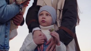 Küçük bir çocuk iki yetişkin tarafından tutuluyor.