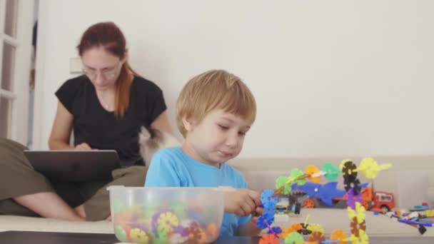 小男孩和建筑商一起玩 他的妈妈在沙发上的笔记本电脑上工作 — 图库视频影像