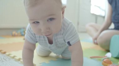 Yerde sürünen ve kameraya bakan küçük bir bebek. Orta çekim