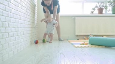 Anne bebeğine yürümeyi öğretiyor. Bebek bir topla oynamak istiyor. Orta çekim