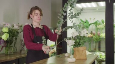 Çiçekçide çiçek düzenleyen bir kadın.