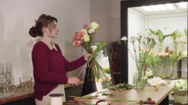 Masadaki vazoda çiçekleri düzenleyen bir kadın.