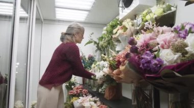 Çiçekçide çiçek düzenleyen yaşlı bir kadın.