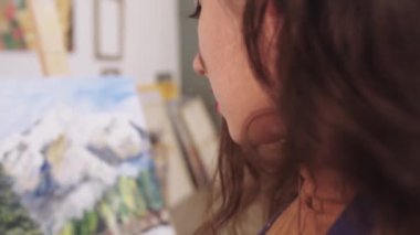 Bir kadın sehpada bir tabloya bakıyor.