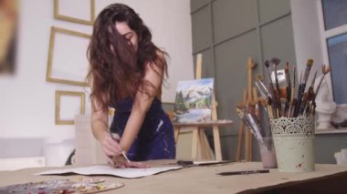 Masaya mavi elbiseli bir kadın resim yapıyor.